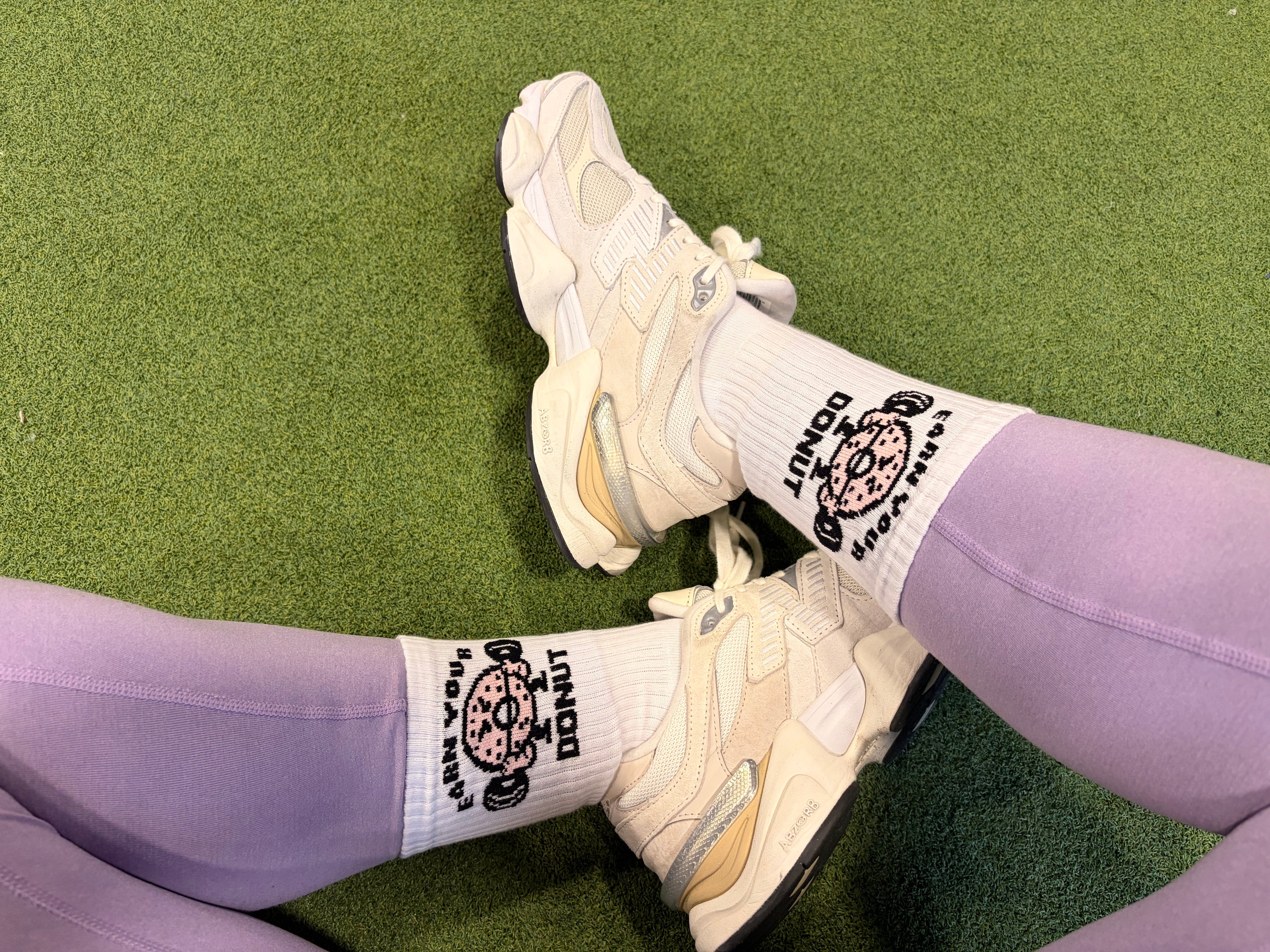 White sneakers and purple leggings with socks on a green grass background