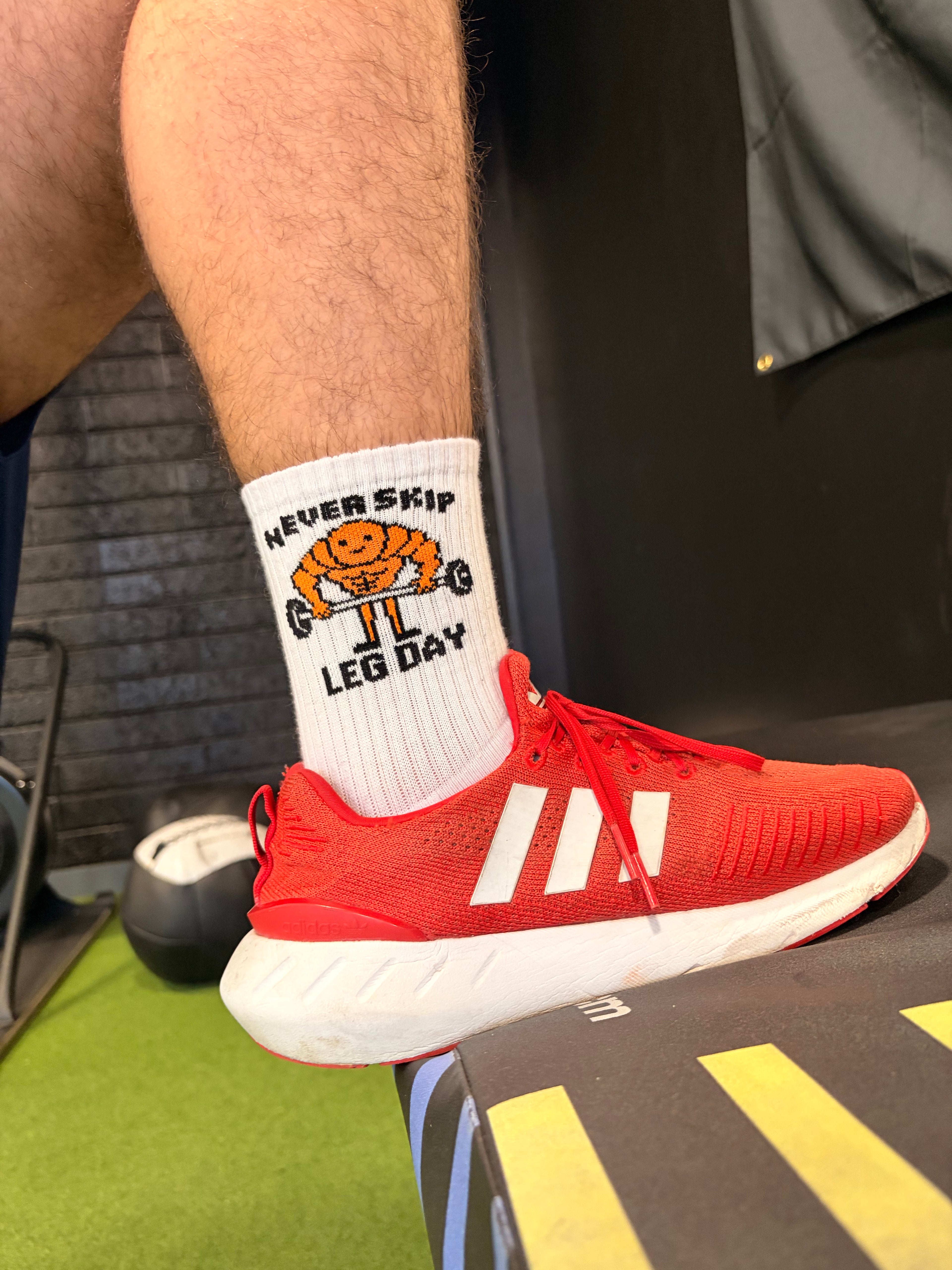 Red Adidas sneaker with a white sock featuring 'Never Skip Leg Day'.