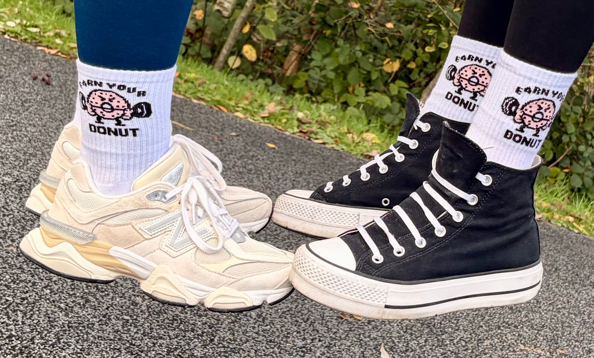 Two pairs of feet wearing socks with 'Earn Your Donut' design, one in white sneakers and the other in black high-top sneakers.